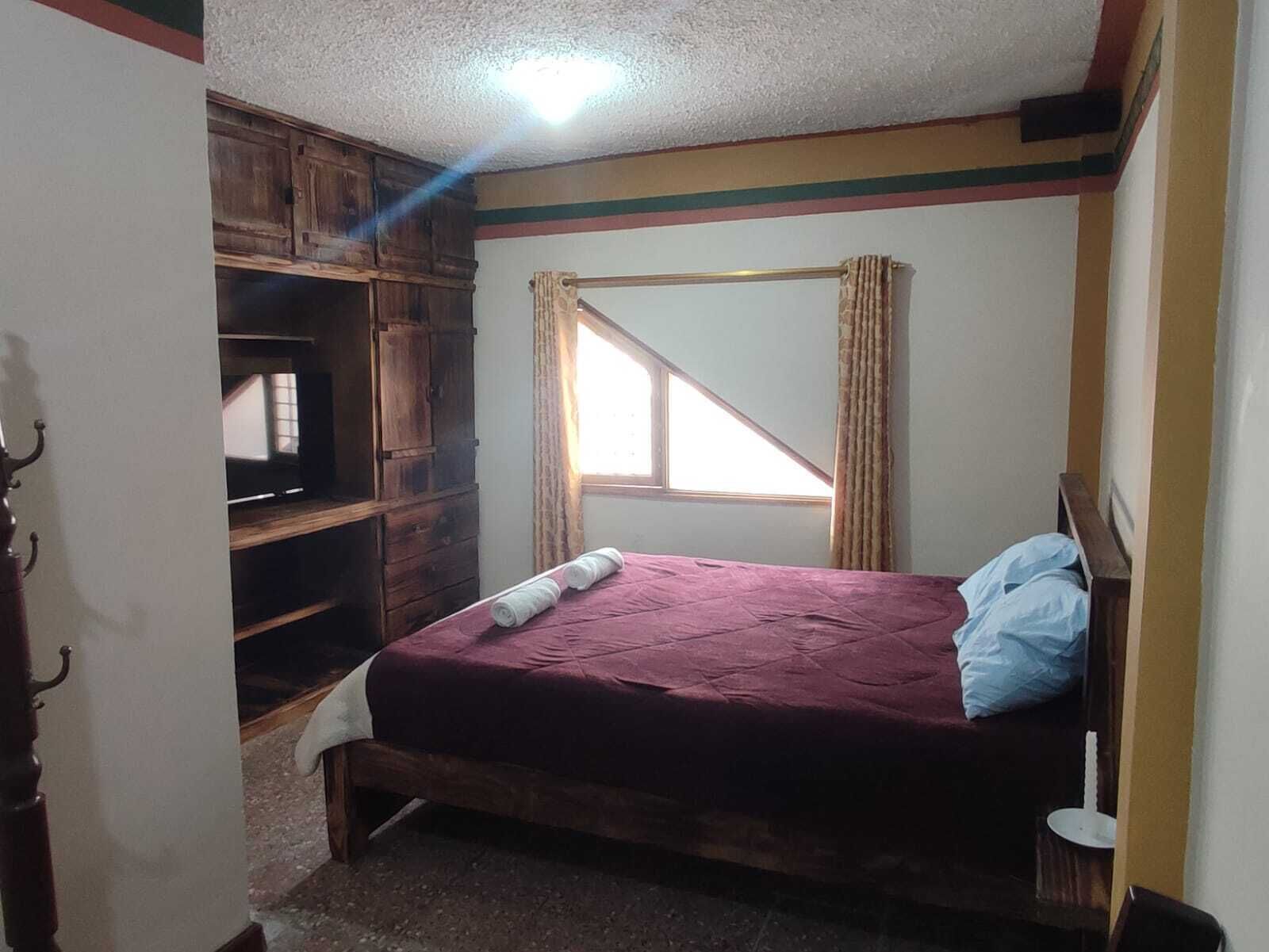 A bedroom with a bed, wooden wardrobe, and a window with curtains.