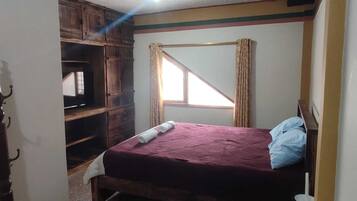 A bedroom with a bed, wooden wardrobe, and a window with curtains.