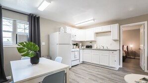 Een moderne keuken met witte kastjes, een koelkast, en een eethoek met een tafel en stoelen.