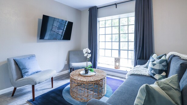 Een moderne woonkamer met een bank, fauteuil en een ronde rieten salontafel met een plant.