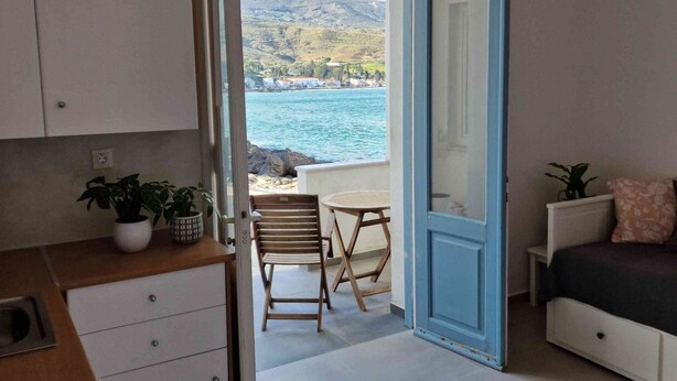 Una habitación con vistas a un paisaje costero, un comedor con una mesa y sillas, y una cama con un almohadón.