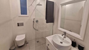 Un baño moderno con ducha acristalada, inodoro, lavabo y espejo.