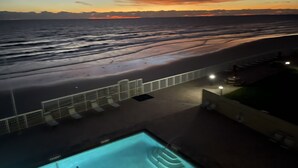 Una piscina con vistas a la playa y al océano al atardecer.