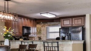 Una cocina con una isla central, sillas de madera oscura, un sofá de cuero y una araña.