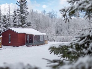 A red cabin with a snow-covered roof, surrounded by snow-laden trees and a clear sky. - Pod Liščím kopcem 2+2 by Interhome (Dolni Branna)
