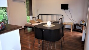 A modern room with a wooden floor, a black round table with a white object on it, a sofa with beige cushions, and a TV mounted on the wall. - Pod Liščím kopcem 2+2 by Interhome (Dolni Branna)