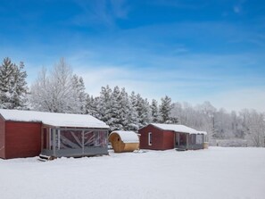A row of red wooden cabins with snow-covered roofs, set against a backdrop of snow-laden trees and a clear blue sky. - Pod Liščím kopcem 2+2 by Interhome (Dolni Branna)