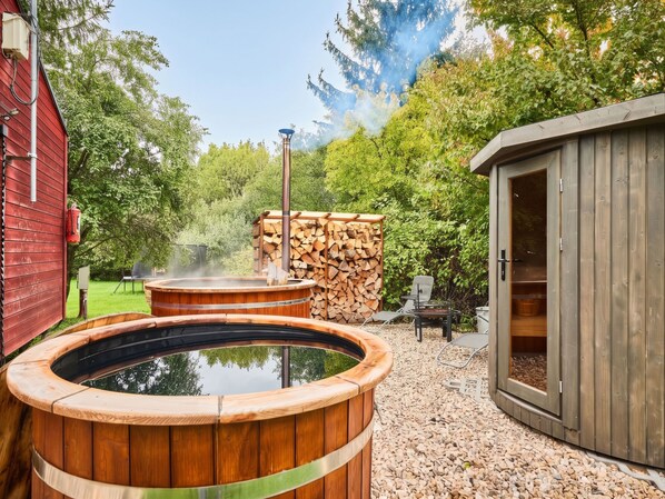 A hot tub area with a wooden deck, a sauna, and a sauna room with a door.