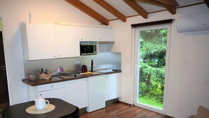 A compact kitchen with white cabinets, a microwave, and a sink. There's a dining table with chairs, and a sliding glass door leading to a green outdoor area. - Pod Liščím kopcem 2+2 by Interhome (Dolni Branna)
