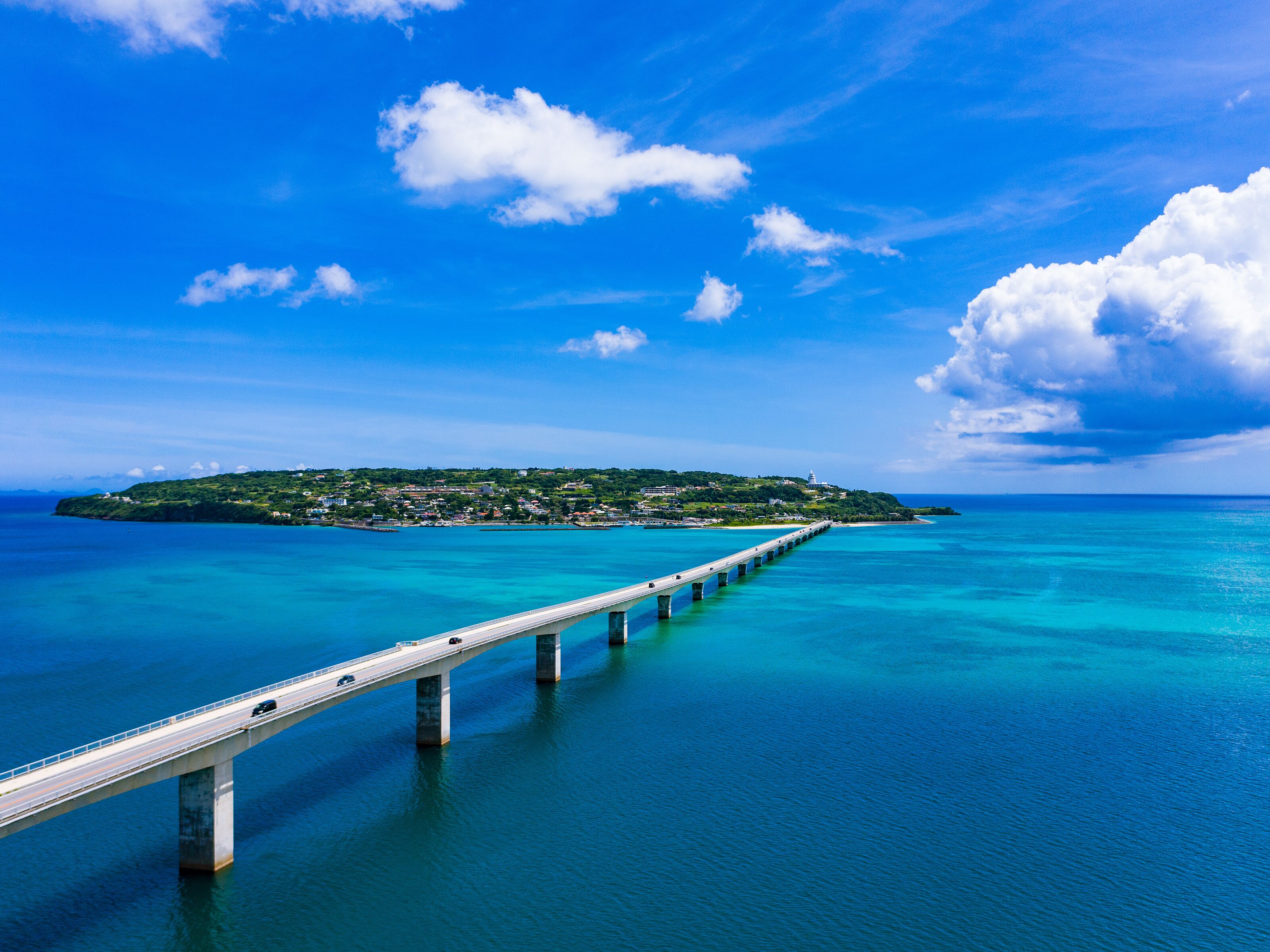 A long bridge over turquoise waters leading to a green island with buildings.