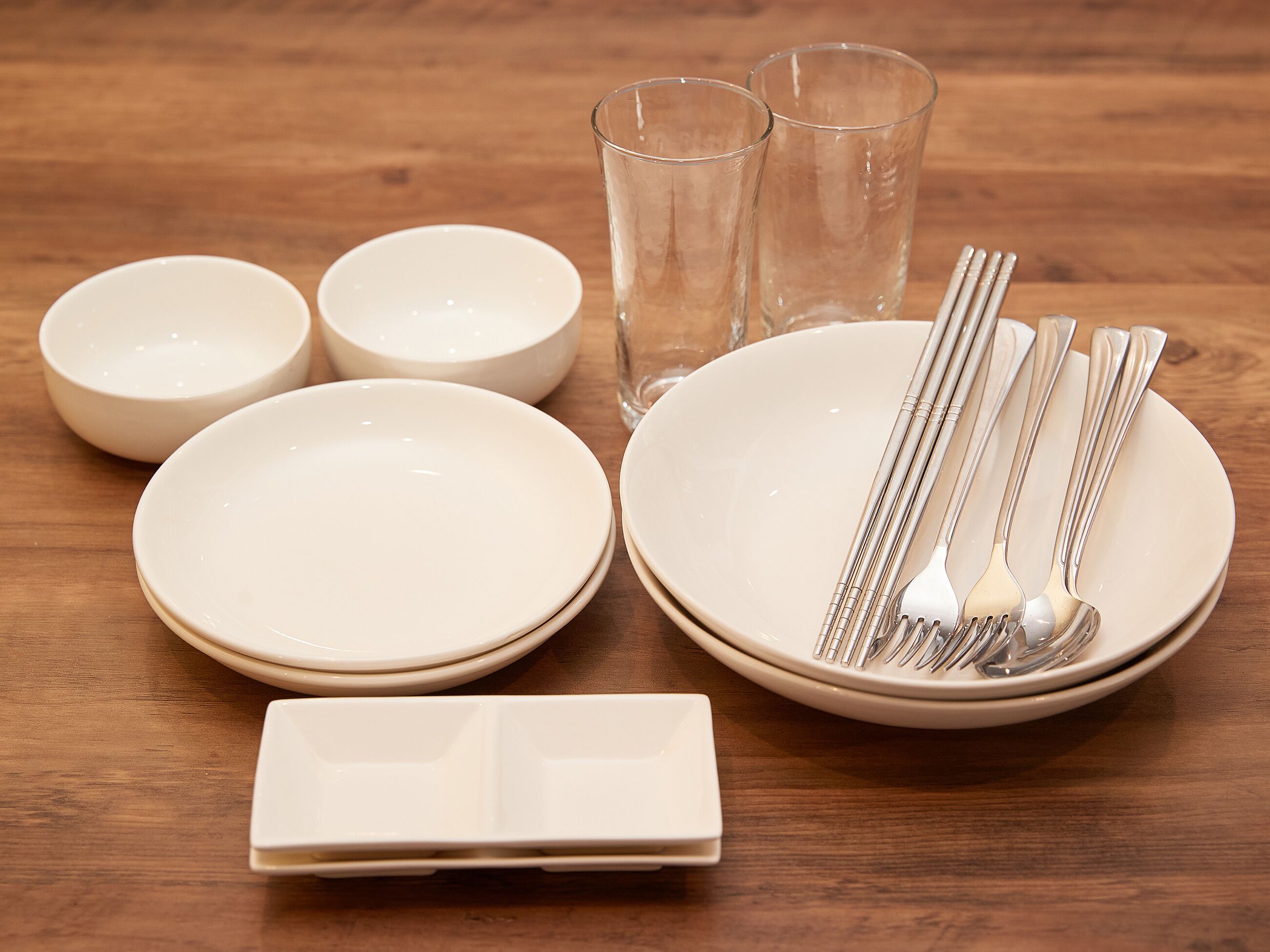 A set of white plates, bowls, and cutlery arranged on a wooden table.