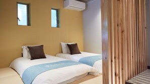 A hotel room with two beds, a window, an air conditioning unit, and a wooden panel on the right. - ADAN RESORT -LANTERN- (Motobu)