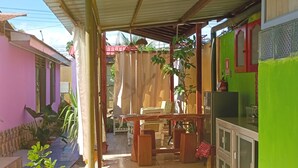 Een overdekt buitengebied met een tafel, stoelen, potplanten en een groene wand.