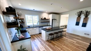A modern kitchen with a central island, bar stools, wooden flooring, and a window providing natural light.