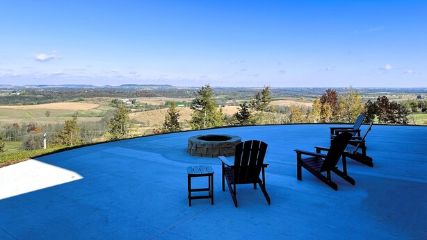A patio with Adirondack chairs and a fire pit overlooking a scenic landscape.