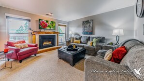 A cozy living room with a fireplace, a red leather sofa, a grey couch, and a coffee table. - On Mountain Time | Upscale Townhome Retreat w/ Cozy Nights & Outdoor Adventure Nearby (Alto)