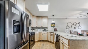 A modern kitchen with a stainless steel refrigerator, wooden cabinets, a granite countertop, and a skylight. - On Mountain Time | Upscale Townhome Retreat w/ Cozy Nights & Outdoor Adventure Nearby (Alto)