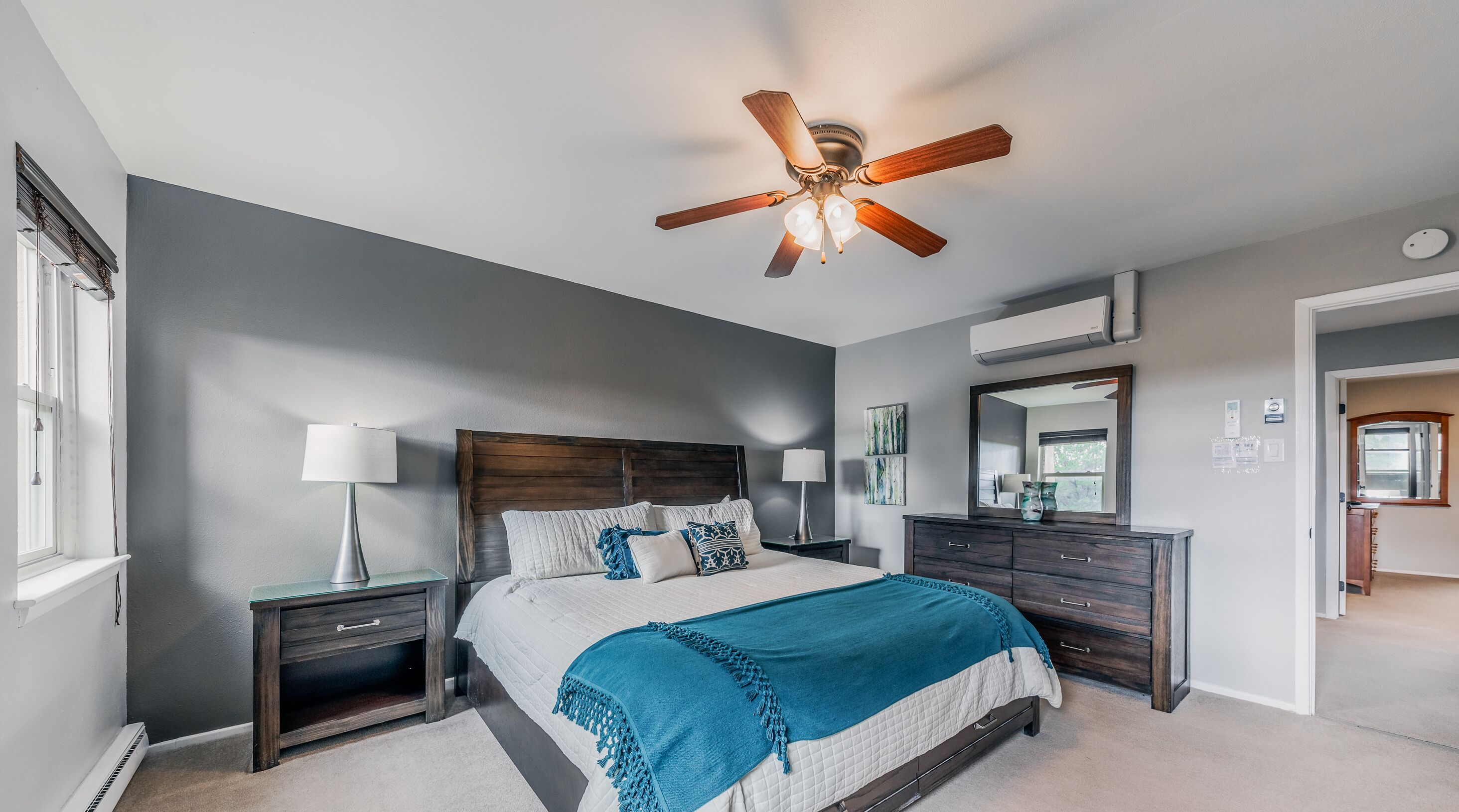 A bedroom with a bed, two bedside tables, a ceiling fan, a dresser, and a mirror.