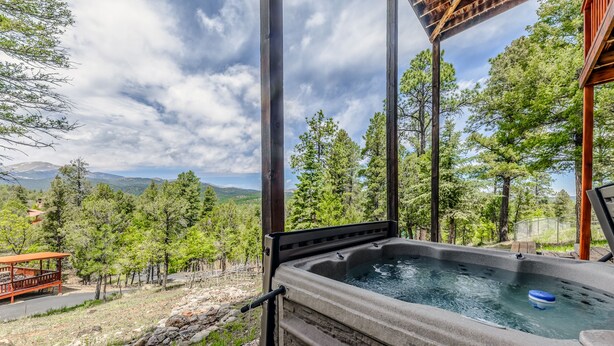 A hot tub with a view of a mountainous landscape, surrounded by trees and a wooden deck.