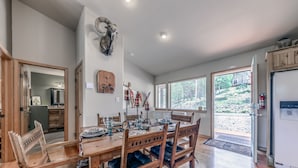 A dining area with a wooden table set for four, surrounded by chairs. A ram head decoration hangs on the wall above the table.
