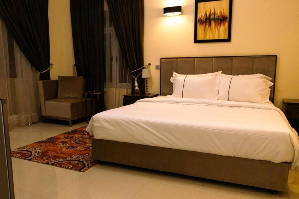 A hotel room with a large bed, a chair, a nightstand, and a painting on the wall.