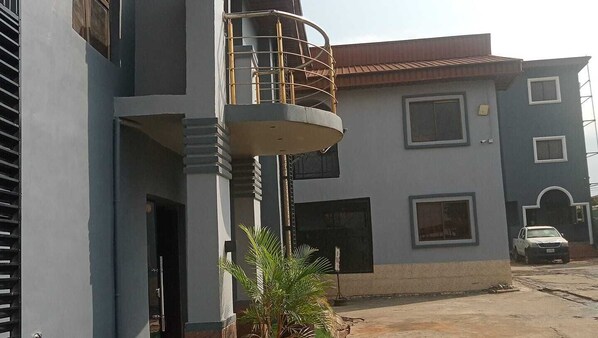 Un edificio residencial de varios pisos con balcón, ventanas amplias y un coche aparcado.
