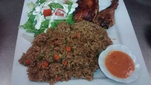 Un plato con arroz frito, un muslo de pollo a la parrilla, una ensalada y un recipiente con salsa.