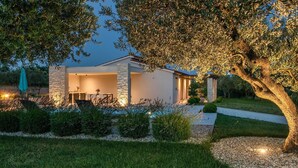 Uma casa moderna com área de pátio, pilares de pedra e um jardim bem cuidado.