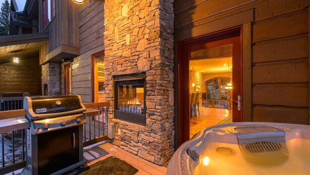 Una chimenea de piedra, una parrilla y un jacuzzi en el exterior de una construcción de madera.