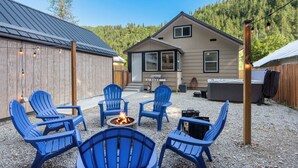 Un espace patio avec des chaises Adirondack bleues, un foyer et une maison dotée d’un toit en métal et d’une terrasse en bois.