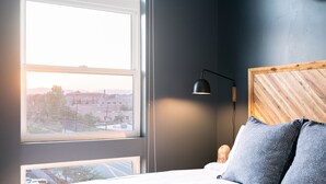A bedroom with a large window, a bed with pillows, a bedside lamp, and a wooden headboard. - (Denver)