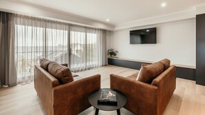 Un salon moderne comprenant un canapé, deux fauteuils, une table basse et un téléviseur fixé au mur.