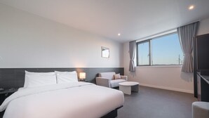 Une chambre d’hôtel moderne, dotée d’un grand lit, d’un canapé, d’une petite table ronde et d’une grande fenêtre avec des rideaux.