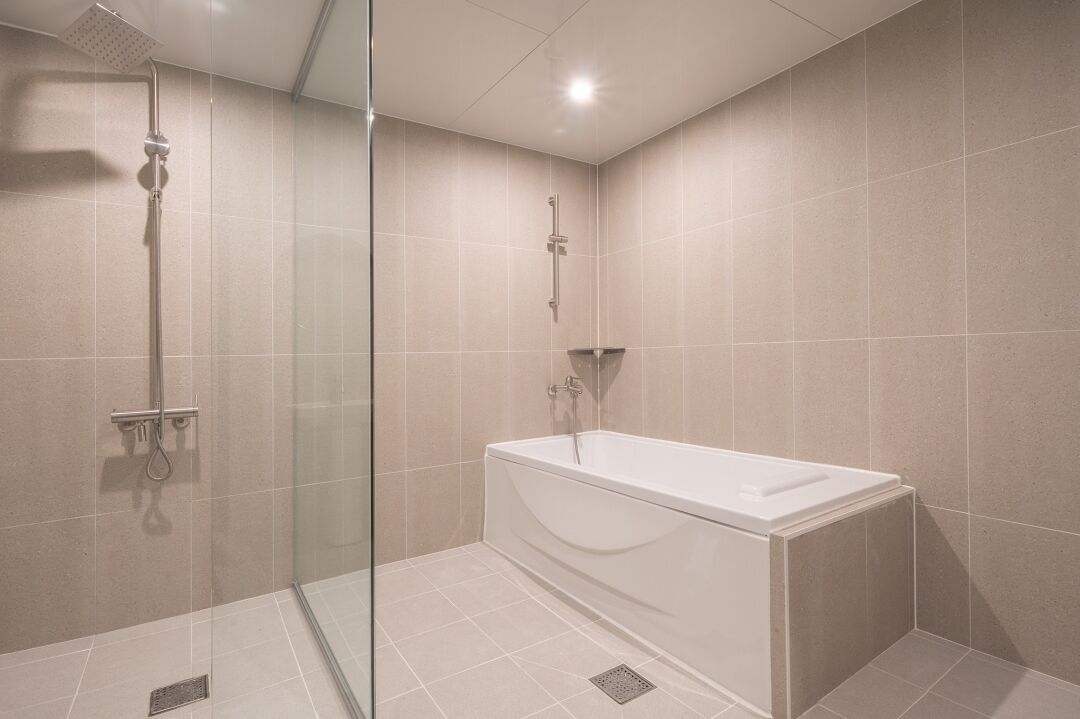 Une salle de bain moderne avec une douche à l’italienne en verre, une baignoire sur pieds et des murs carrelés.