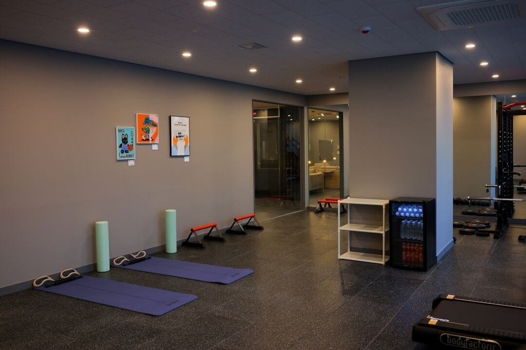Une salle de sport équipée de tapis de sol, de bancs, d’un tapis de course et d’un distributeur d’eau.
