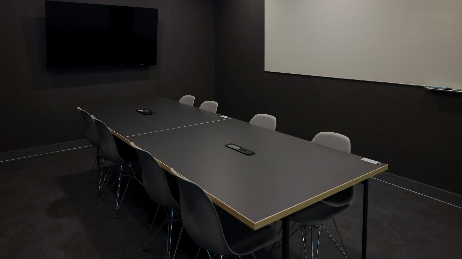 A conference room with a long table, six chairs, a projector screen, and a TV on the wall.