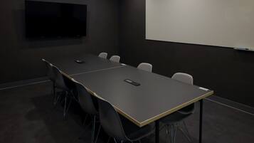 A conference room with a long table, six chairs, a projector screen, and a TV on the wall.