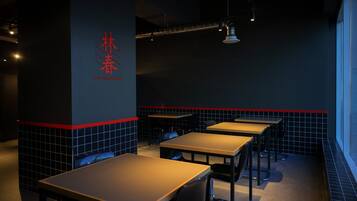 A restaurant interior with tables and chairs, a dark wall with red accents, and a logo on the wall.