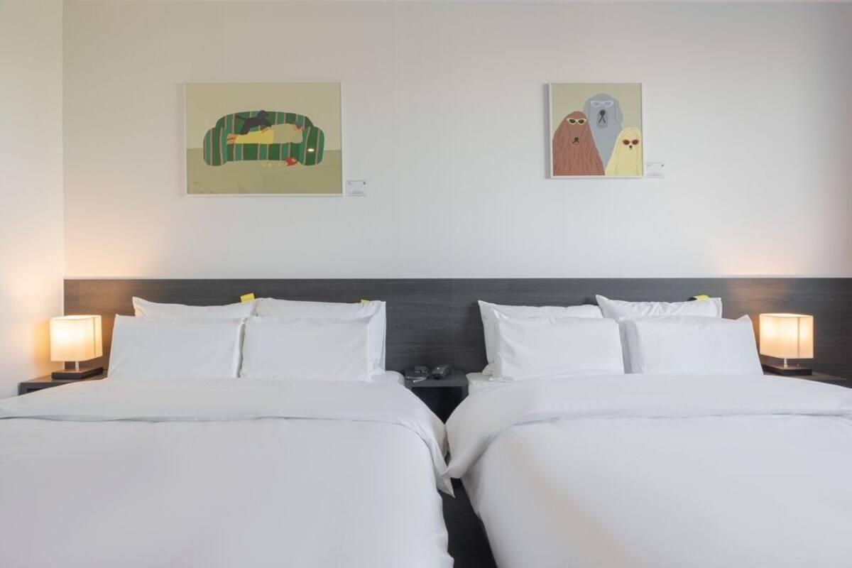 Une chambre d’hôtel avec deux lits, une tête de lit sombre et deux lampes de chevet.