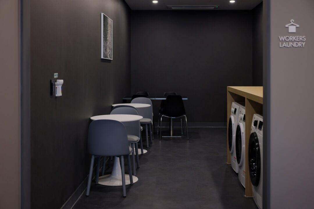 A laundry room with a row of washing machines, a table, and several chairs.