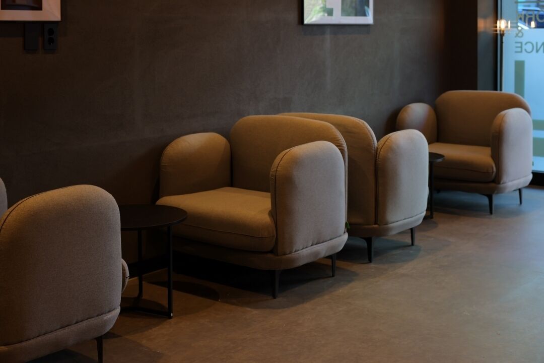 A row of four armchairs with a small table in between, against a dark wall with a framed picture.