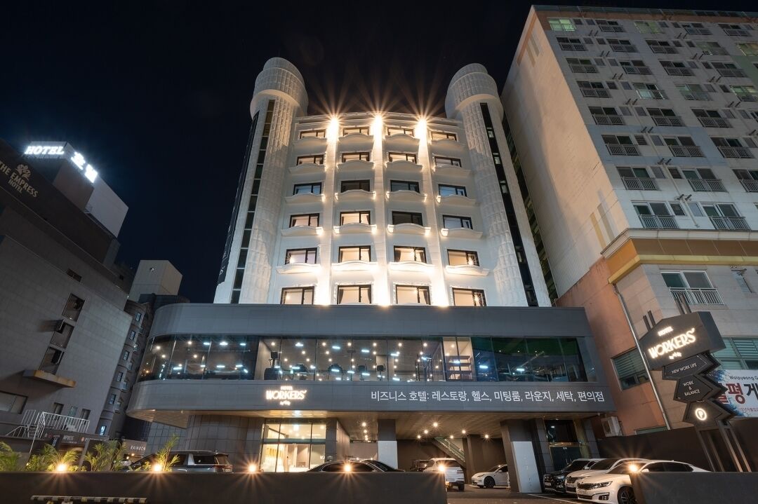 A multi-story hotel with a modern design, featuring a prominent entrance with glass railings and a sign for 'WORKERS'.