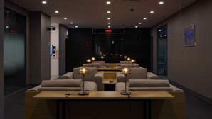 Un espace de détente moderne avec des canapés et des tables, un comptoir d’accueil et un écran numérique.