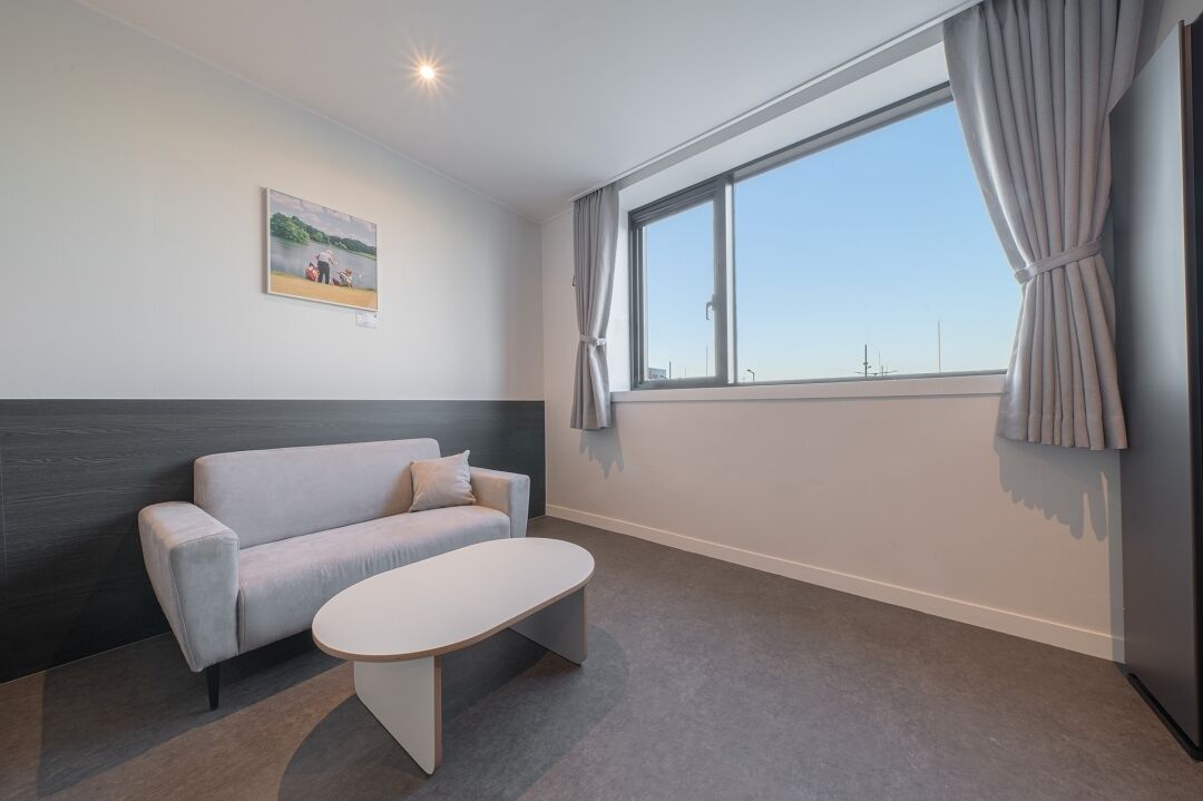 Una habitación de hotel moderna con un sofá gris, una mesita de café blanca y un ventanal con cortinas.