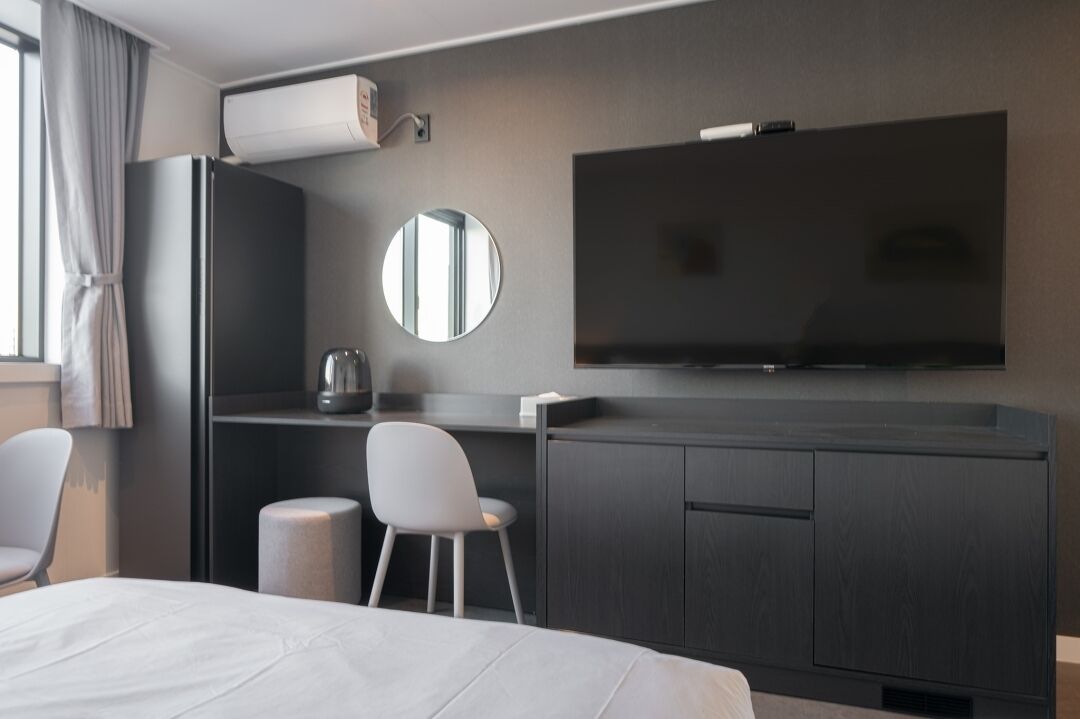 A modern hotel room with a bed, a desk, a chair, a television, and a mirror.
