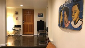 Een woonkamer met een bruine leren bank, een houten deur, een zwarte tv-meubel en een aan de muur hangend schilderij.