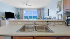 A kitchen with a double sink, a ceiling fan, a TV, and a view of the ocean. - Seychelles 703 | Beach Chair Service Included at this 7th Floor, Oceanfront Condo (Panama City Beach)