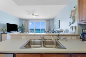 A kitchen with a double sink, a ceiling fan, a TV, and a view of the ocean.