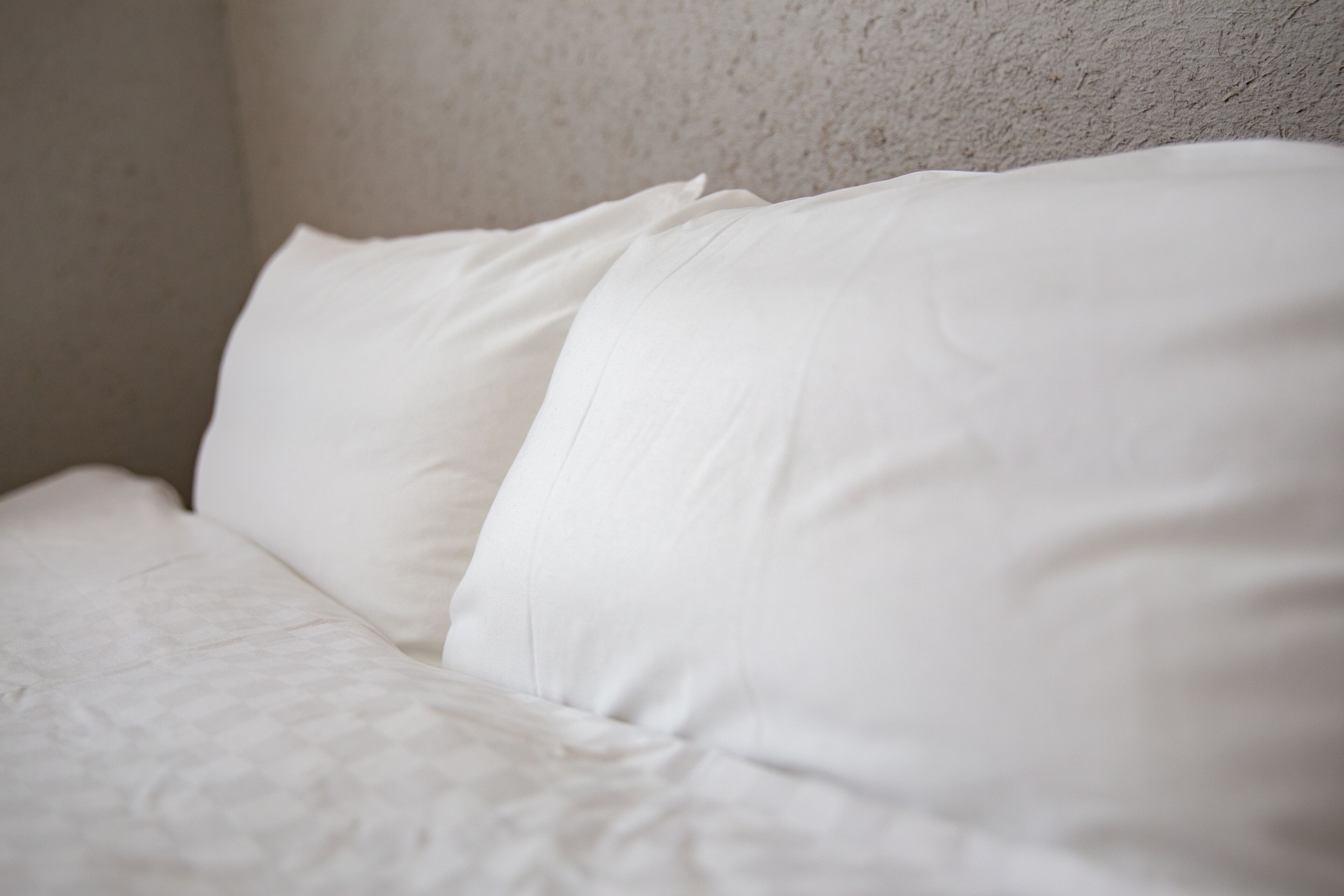 A close-up of a white pillow against a textured wall.