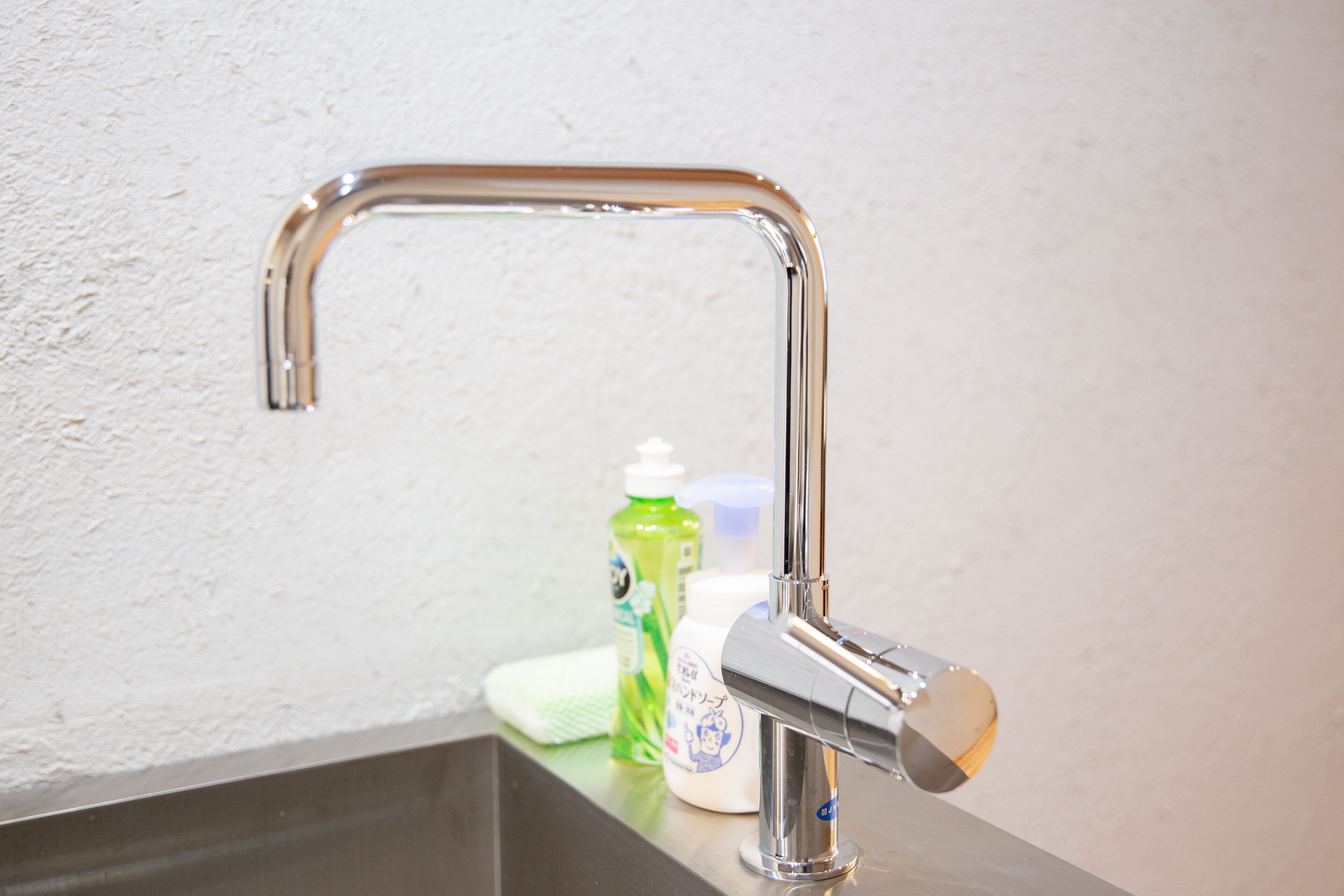 A bathroom sink with a chrome faucet, a green bottle of hand soap, and a white bottle of lotion.